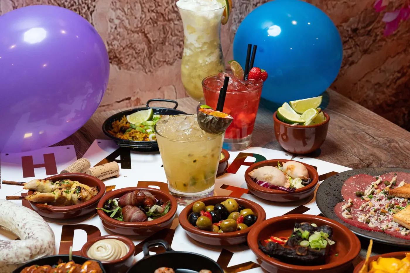Een feesttafel vol tapas en cocktails, met paarse en blauwe ballonnen