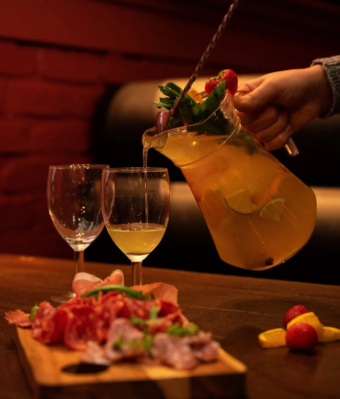 Witte sangria wordt uit een kan met vers fruit ingeschonken, naast een plank met vleeswaren